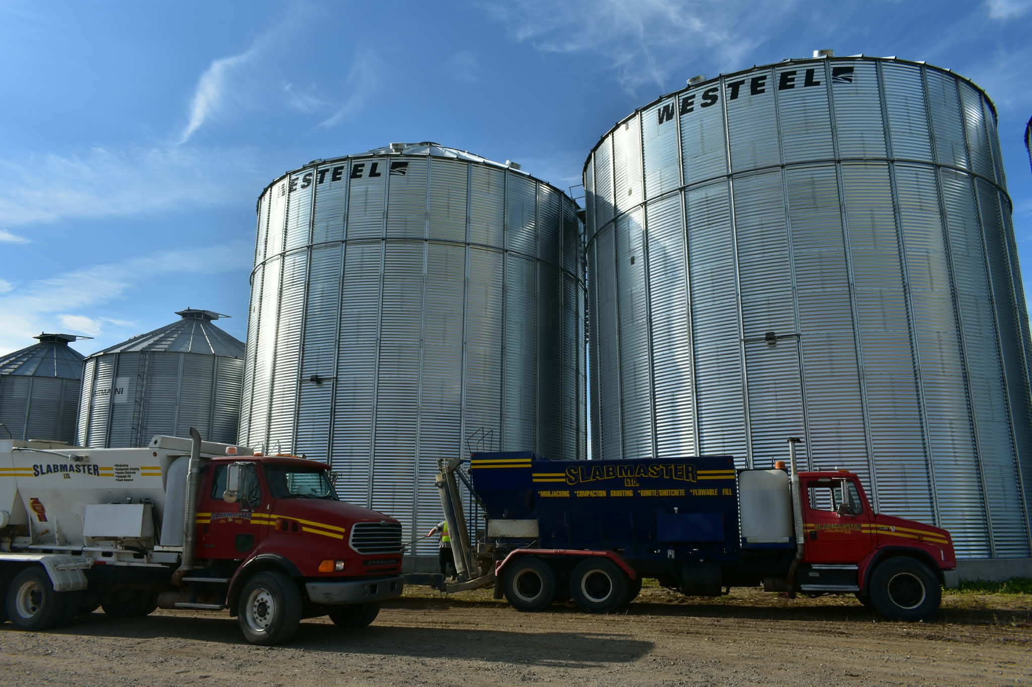 Backyard View With A Raised Wooden Deck Attached To A House, Leading To A Small Shed In The Background.
